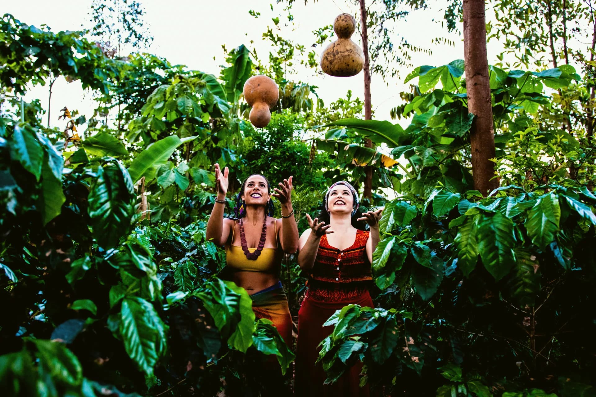 Duas mulheres em meio à mata, brincando com os agbês pendurados nos galhos