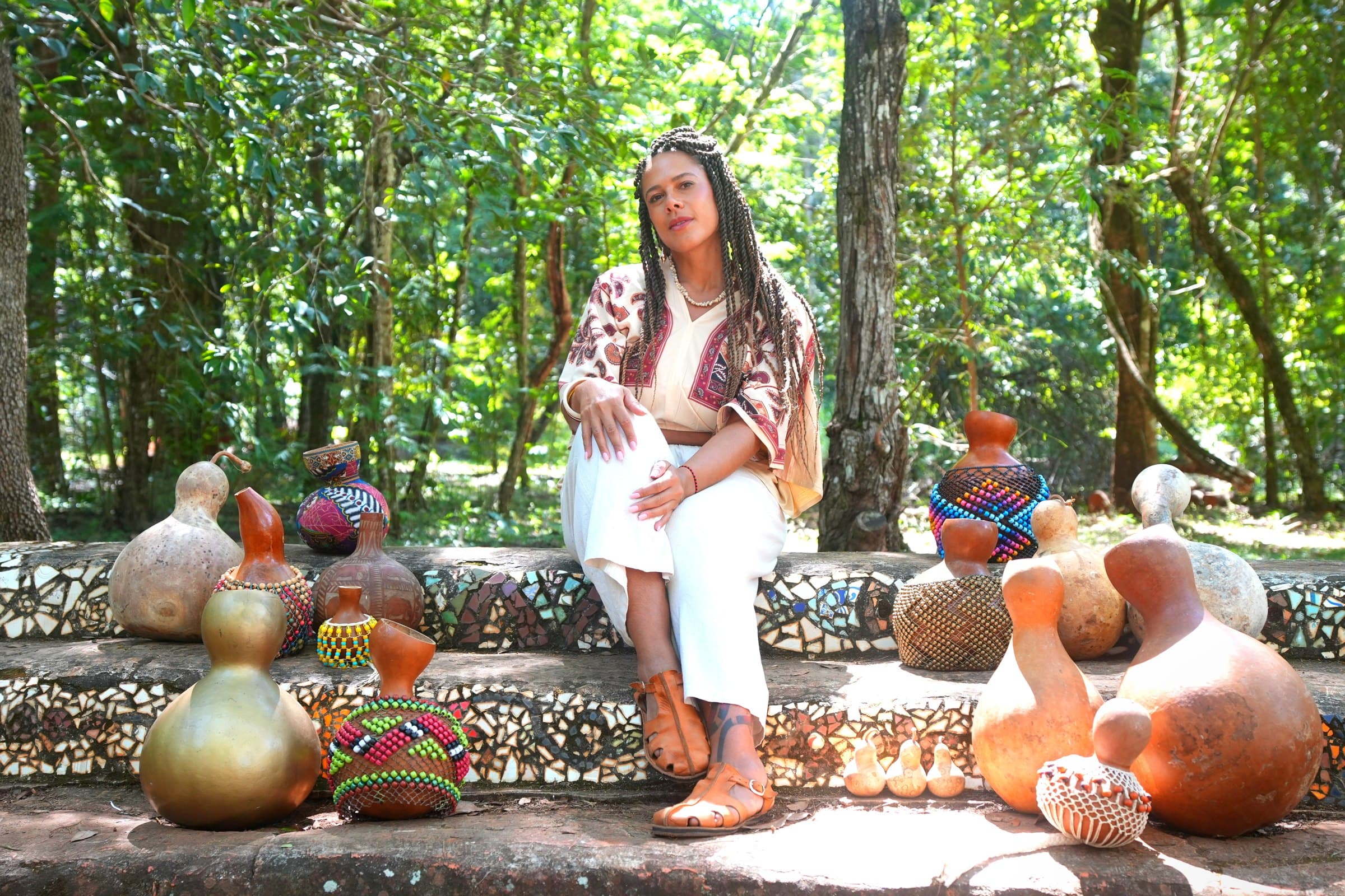 Gio Paglia sentada na arquibancada de pedra com os agbês espalhados, no Parque Olhos Dágua