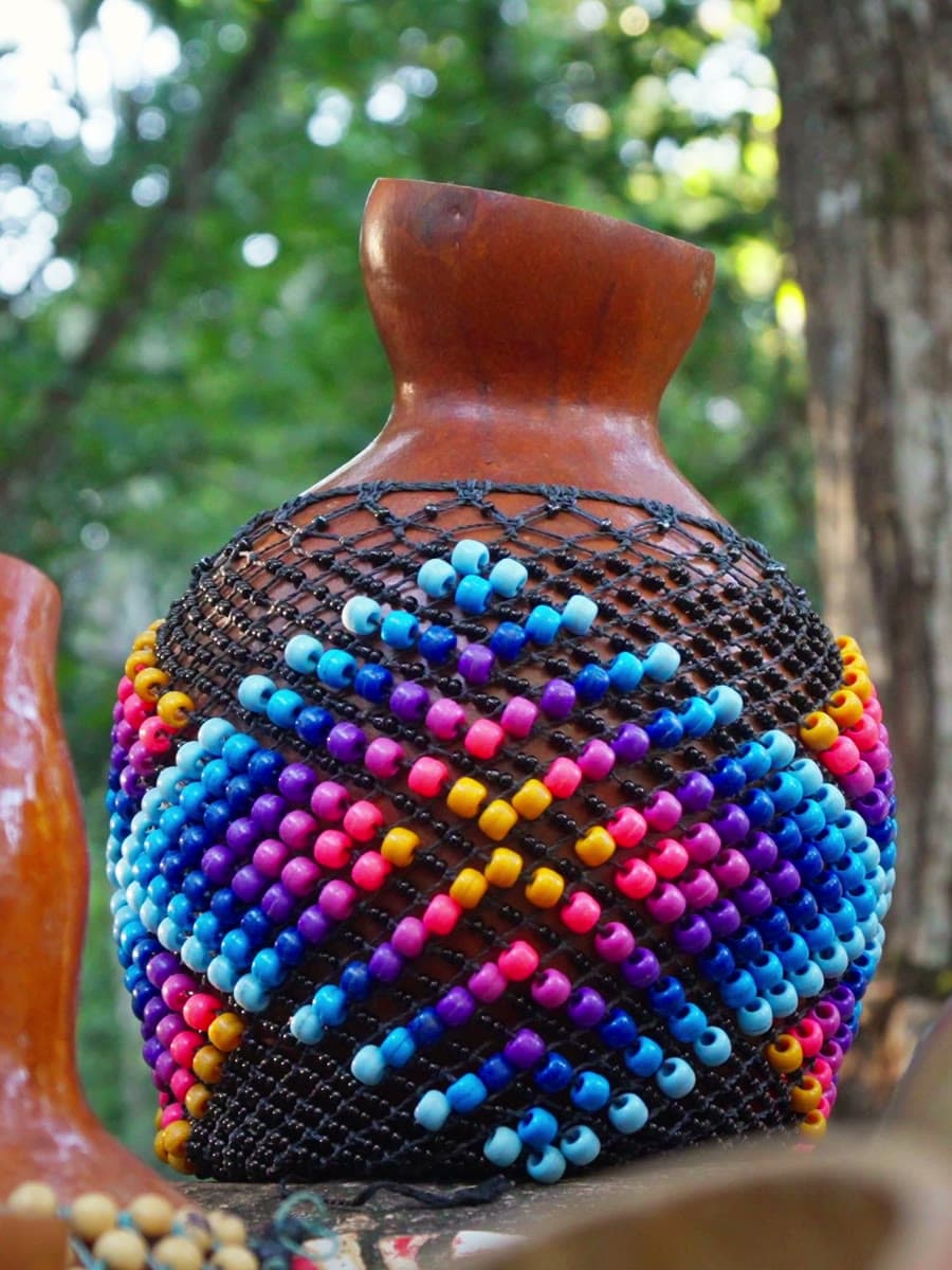 Agbê com miçangas em padrão colorido, na mata